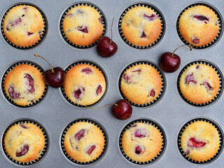 Baking muffins with cherries. Baking tray with paper cases with freshly baked muffins and fresh fruits