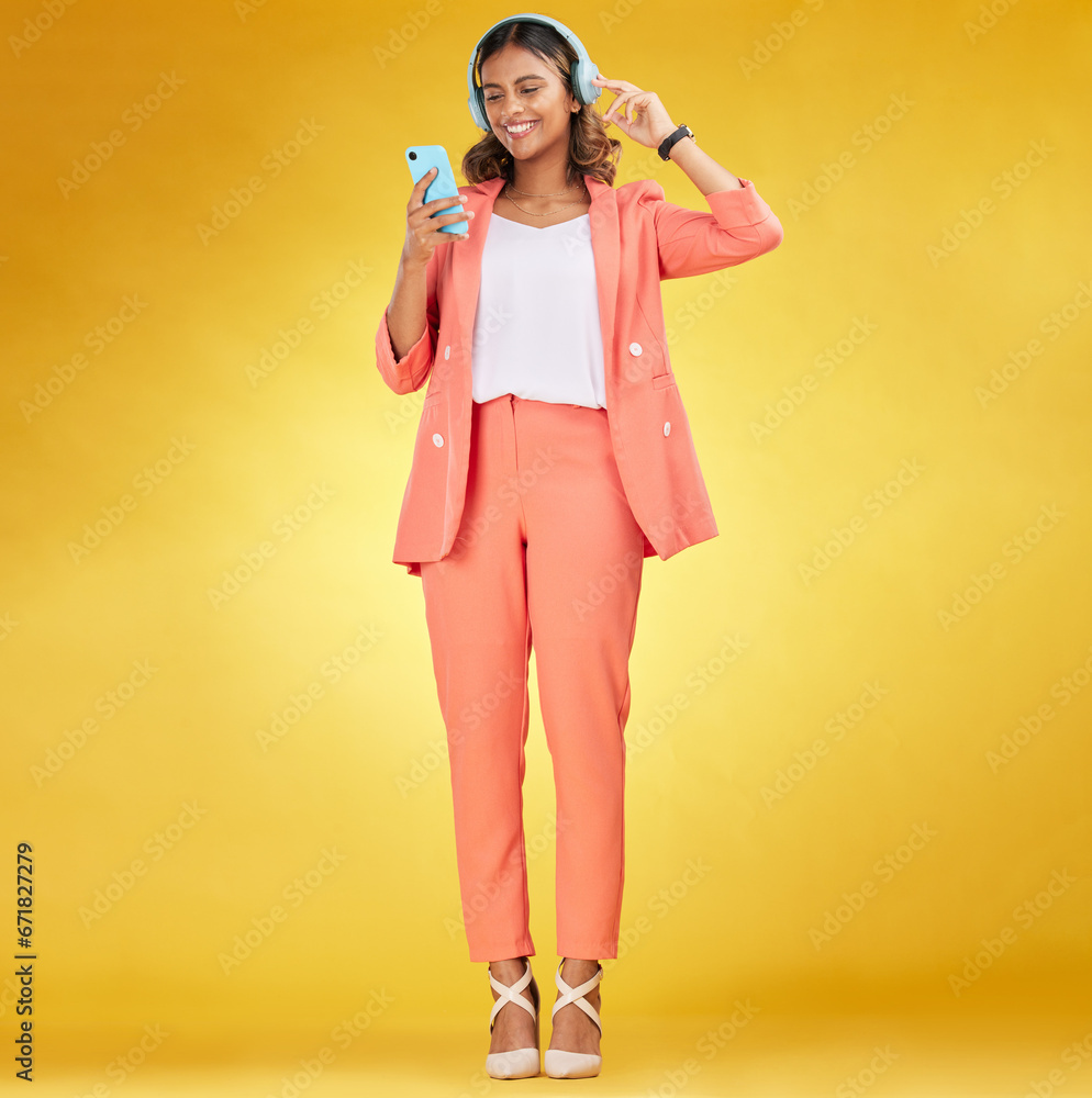 Wall mural Happy woman, headphones and phone for music in studio for fashion, podcast and app on yellow background. Indian model, style and listening to audio technology, streaming mobile sound and online radio