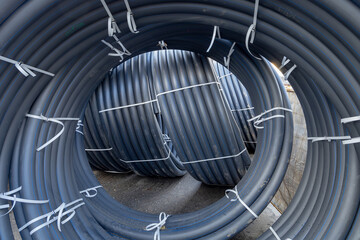 Several rolled up small diameter polyethylene pipes for laying high voltage electric cables underground. Warehouse or construction site or storage. Black pipes coiled into rings or spool or coils