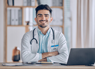 Happy, portrait and man doctor at desk in a healthcare, medical and hospital office. Smile, male professional and surgeon worker with arms crossed and computer feeling confident and pride in clinic - Powered by Adobe