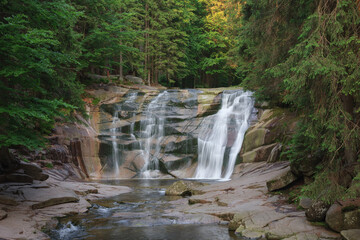 Mumlava waterfall, in the foreground  stone riversides . Mountain river Mumlava, Krkonose national park, Czech Republic, summer afternoon.