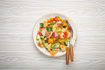 Traditional Levant dish Fattoush salad, Arab cuisine, with pita bread croutons, vegetables, herbs. Healthy Middle Eastern vegetarian salad, rustic wooden white background top view.