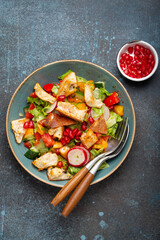 Traditional Levant dish Fattoush salad, Arab cuisine, made with pita bread croutons, vegetables and herbs. Healthy Middle Eastern vegetarian salad on plate, rustic dark blue background top view.