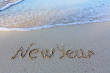 Word new year handwritten on the caribbean sand.