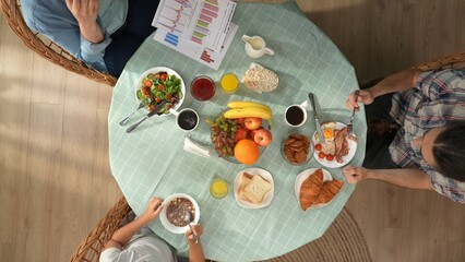 Top view of family sitting at the table eating breakfast, close up of mother working talking on smartphone, dad and girl unhappy.