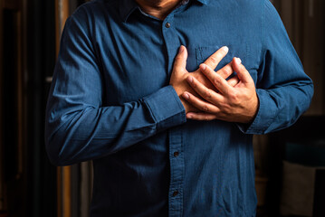 Heart attack. Man in blue shirt clutching his chest from acute pain. Heart attack symptom. Severe heartache, man suffering from chest pain, having heart attack or painful cramps, pressing on chest