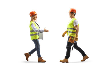 Full length profile shot of a female engineer walking and greeting a construction worker