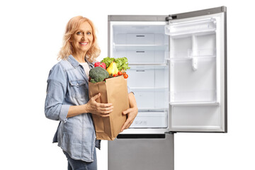 Mature woman with a grocery bag next to an open fridge