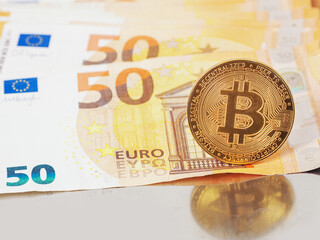 Gold shiny bitcoin with flare, Euro banknotes out of focus in in the background. Economy and financial background. Grey color background. Vertical image. Popular cryptocurrency or payment system.