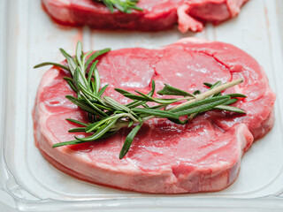 Juicy uncooked boneless lamb leg steak with green fresh rosemary on plastic tray. Uncooked high quality meat product with rich taste and vivid color.