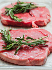 Juicy uncooked lamb leg steak with green fresh rosemary on plastic tray. Uncooked high quality meat product with rich taste and vivid color.