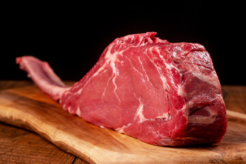 Fresh uncooked tomahawk steak on the bone on wooden cutting board and table and black background....