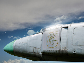 Military war jet airplane tail with Ukrainian air defense logo against blue sky. Old, worn out and rough shiny metal surface. Heavy duty airplane with many combat missions