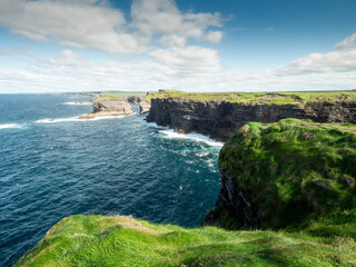 Fototapeta na wymiar Stunning nature scene with cliffs, Atlantic ocean and low cloudy sky on sunny day. Kilkee area, Ireland. Travel, tourism and sightseeing concept. Irish landscape and coastline.