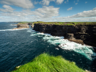 Edge of a cliff and powerful ocean hits rough stone coastline. low cloudy sky, warm sunny day....