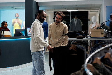 Clothing store smiling client and assistant discussing apparel style while browsing through rack. African american man showing outfit to mall customer and giving fashion advice