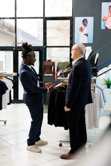 African american worker helping client with formal suit in clothing store, customer looking to buy modern clothes. Elderly client buying fashionable merchandise and trendy accessories in showroom