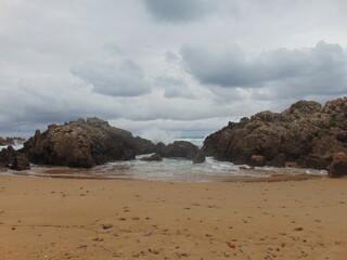 Olas llegando a la playa abriéndose paso entre las rocas un día nublado en una playa de Cantabria 
