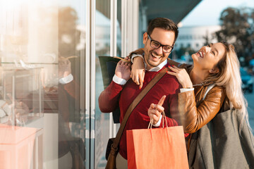 Attractive blonde girl hugging her partner and feeling happy. Handsome smiling man holding shopping bags and feeling close with his girlfriend.