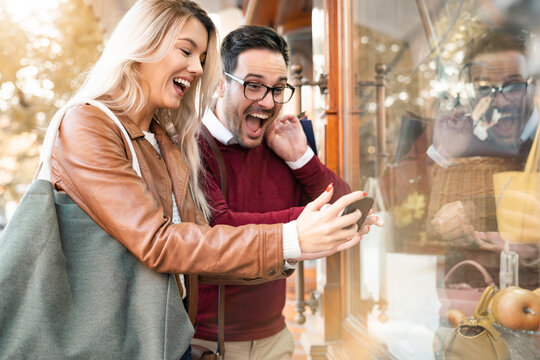 Surprised and excited young couple looking at store window on Black Friday sale.