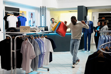 Excited african american shopaholic carrying shopping bags and dancing in clothing store. Fashion boutique happy cheerful client holding packages with apparel and having fun - obrazy, fototapety, plakaty