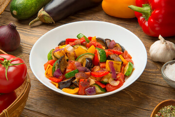 Ratatouille salad in a porcelain salad bowl on a rustic wooden table with ingredients.  - 671861606