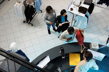 Diverse people waiting in line to pay for selected clothes at department mall checkout desk top view. African american man taking shopping bag from cashier at store cash register - obrazy, fototapety, plakaty