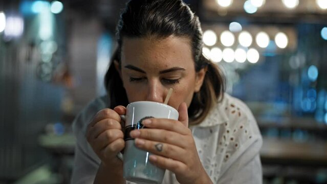 Beautiful young hispanic woman drinking coffee sitting at cafeteria