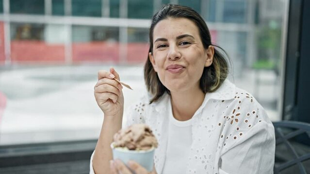 Beautiful young hispanic woman eating ice cream smiling at cafeteria