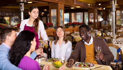 Fototapeta na wymiar Group of joyous friends enjoying evening meal at cozy restaurant
