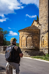 Fototapeta premium lone male hiker walking on the road, taking the opportunity to do some sightseeing by visiting an ancient Romanesque monument along the way