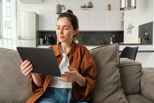 Portrait Of Female Model Reading On Digital Tablet E-book, Watching Tv Series On Her Gadget Application, Sitting In Living Room At Home