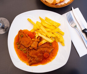 There is hot lunch on tablecloth of table. Juicy pork stew in sauce gravy with fried potato slices