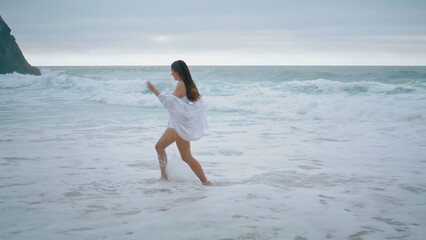 Playful girl running sea waves enjoying cloudy weekend. Woman jumping on beach.