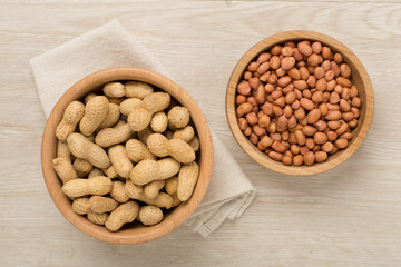 Peeled and unpeeled peanuts on wooden background, top view