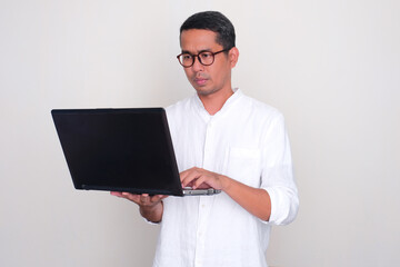 Adult Asian man looking to his laptop with serious face expression