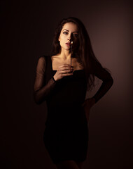 Go to hell. Beautiful makeup female model holding in hand the candle with fire at shadow dark night...