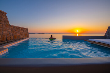 Tourist enjoys at the infinity swimming pool villa at sunset time, Mykonos, Greece