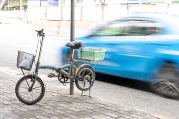 Obraz premium The bicycle parked on a kickstand on the sidewalk next to a busy road, Bangkok, Thailand