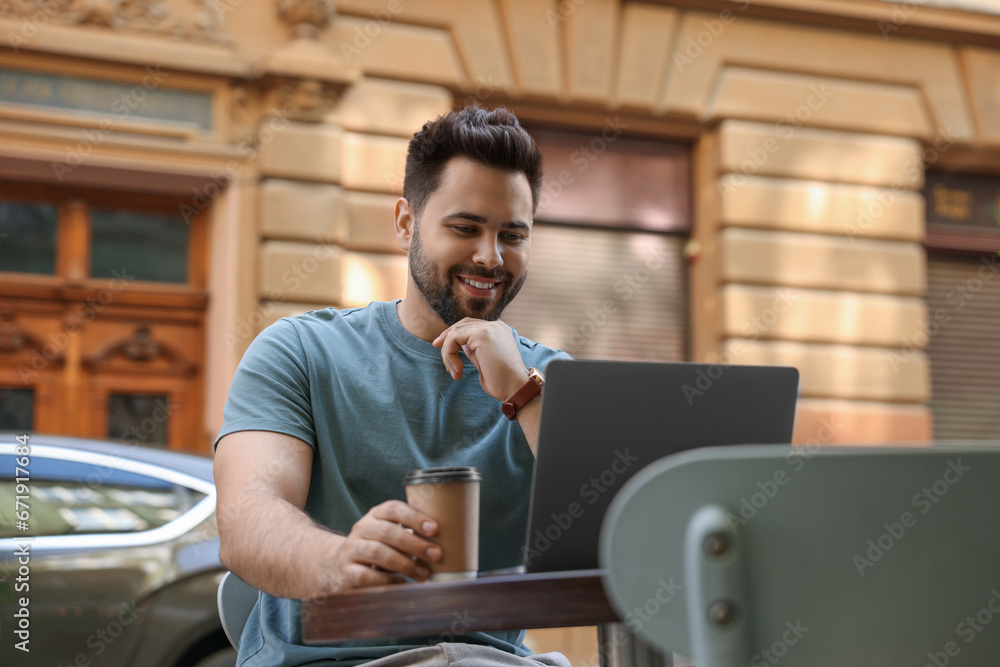 Canvas Prints Handsome young man with cup of coffee working on laptop at table in outdoor cafe