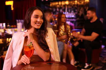 Friends spending time together in bar. Beautiful woman with fresh alcoholic cocktail at table, space for text