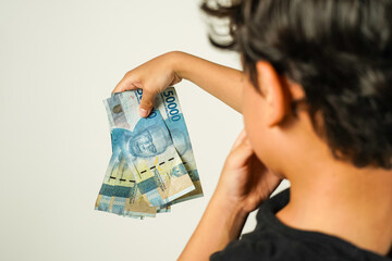 asian boy holding rupiah money in front of him, white background, isolated