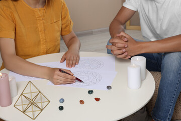 Astrologer showing zodiac wheel to client at table indoors, closeup