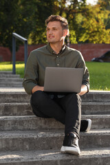 Obraz premium Handsome man with laptop sitting on concrete stairs outdoors