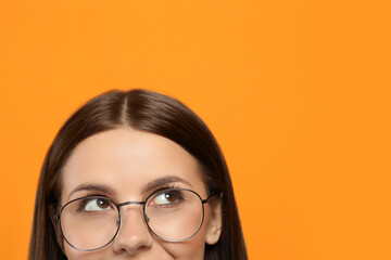 Woman in stylish eyeglasses on orange background, closeup. Space for text
