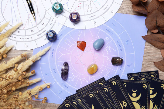 Zodiac wheels, tarot cards, astrology dices and gemstones on wooden table, flat lay