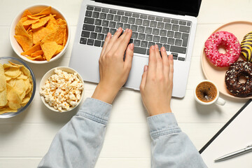 Bad eating habits. Woman using laptop surrounded by different snacks at white wooden table, top view - obrazy, fototapety, plakaty