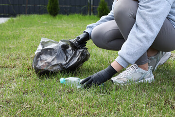 Woman with trash bag picking up plastic bottle outdoors, closeup. Recycling concept