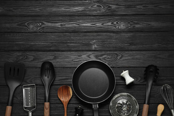 Set of different kitchen utensils on black wooden table, flat lay with space for text