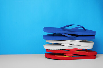 Stack of different flip flops on white table against light blue background, space for text